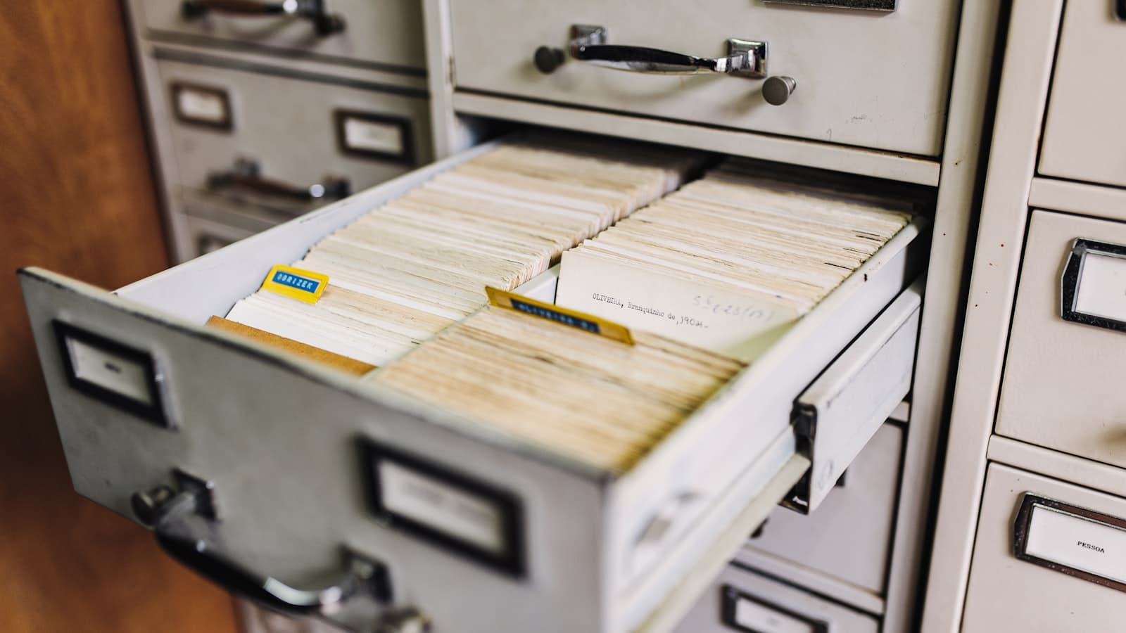 Editorial photograph of three vintage steel filing cabinets standing in a row, one illuminated by a beam of cool blue light from above.