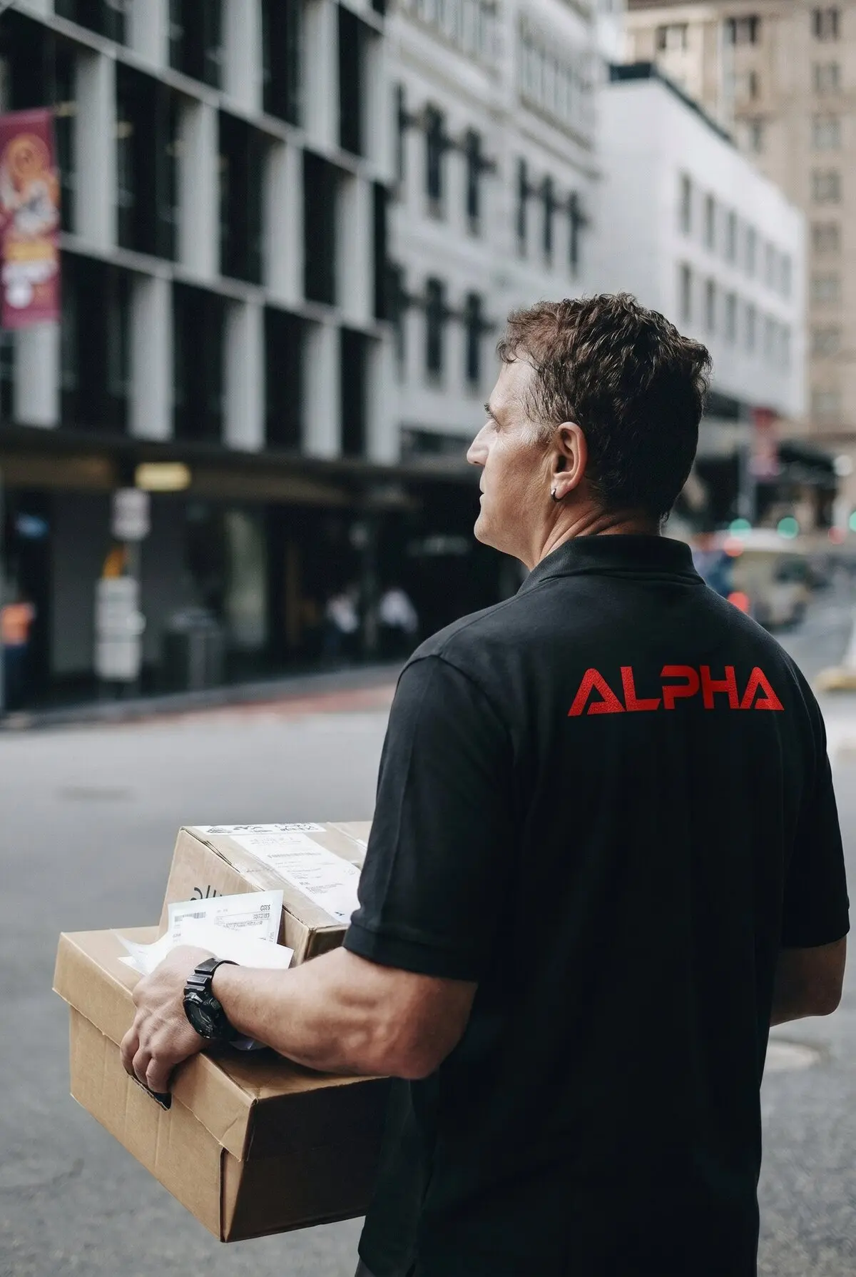 Alpha Transit Services driver in a branded polo carrying packages on a city street