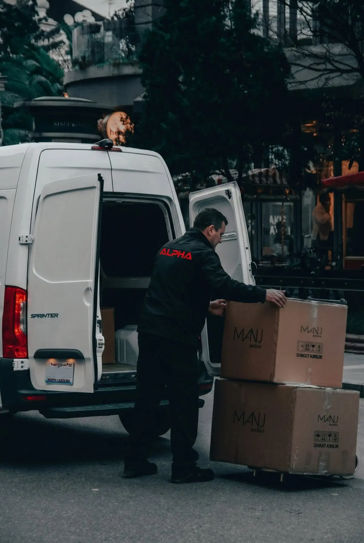 Alpha Transit Services driver in a branded jacket loading freight from a Sprinter van